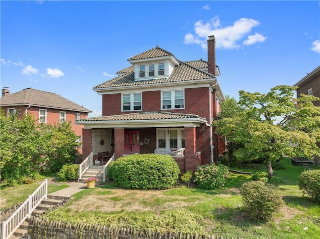 view of front of property featuring a front lawn, a tile roof, a porch, brick siding, and a chimney