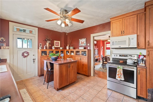 kitchen featuring electric range, light tile patterned flooring, white microwave, and brown cabinets