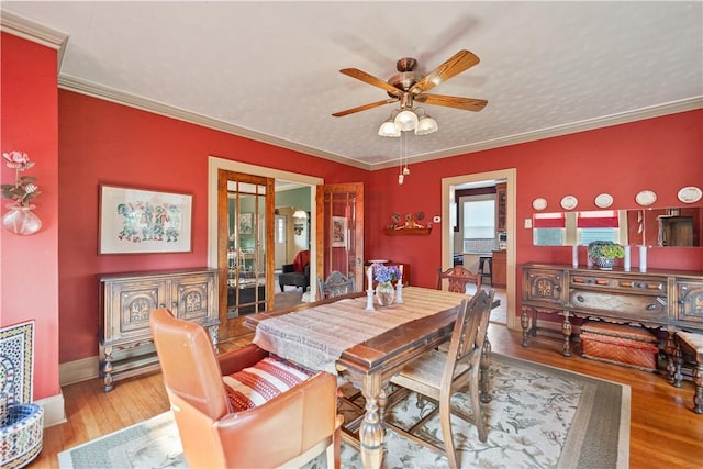 dining room with a ceiling fan, wood finished floors, baseboards, a textured ceiling, and crown molding