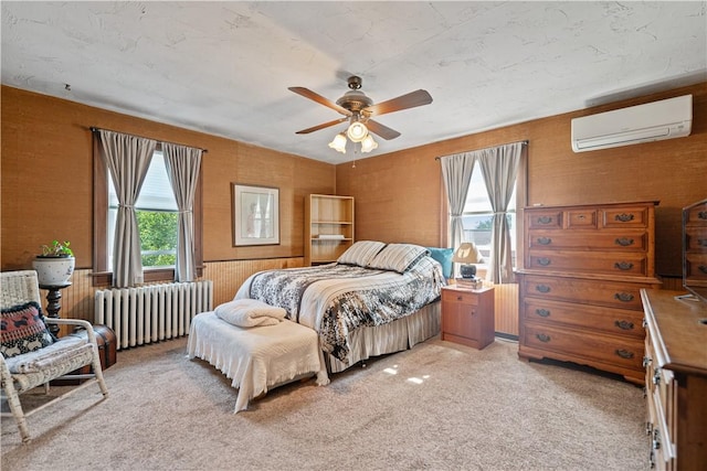 bedroom with a wall mounted air conditioner, light colored carpet, multiple windows, and radiator