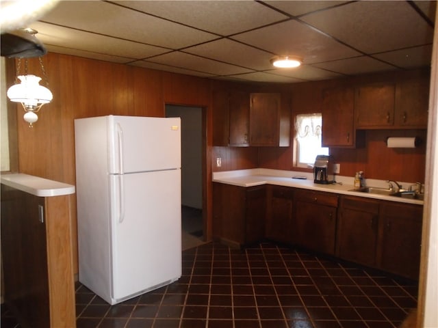 kitchen with dark tile patterned floors, sink, a drop ceiling, wood walls, and white fridge