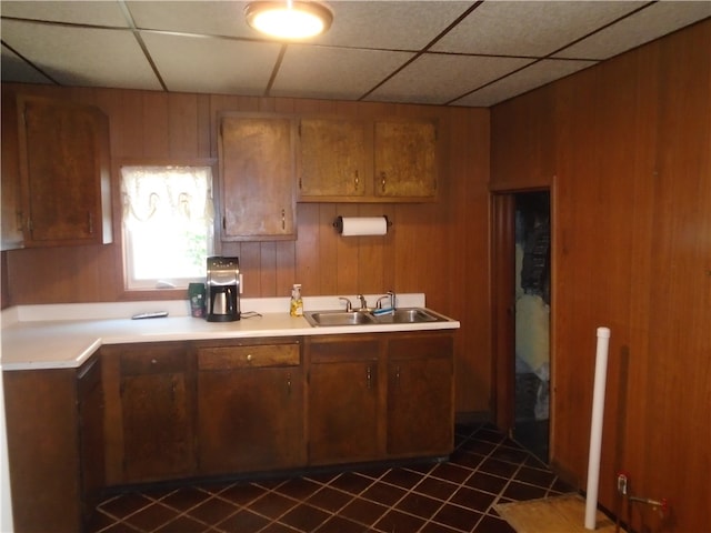 kitchen with a drop ceiling, sink, wooden walls, and dark tile patterned flooring