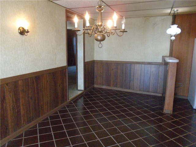 unfurnished room featuring wood walls, a chandelier, and tile patterned floors