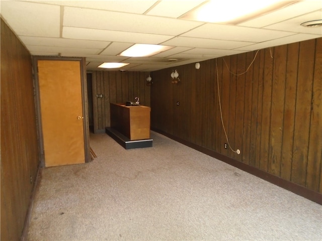 basement featuring wood walls, light carpet, and a paneled ceiling