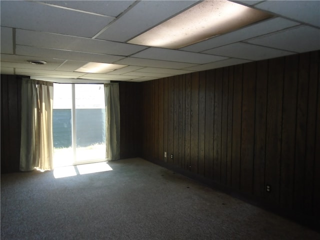 empty room featuring wood walls, carpet floors, and a paneled ceiling