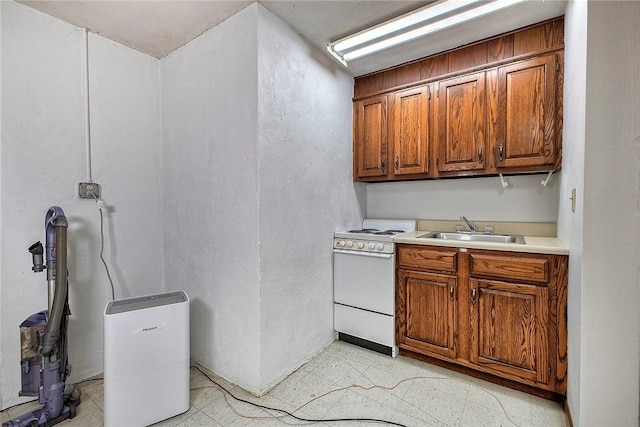 kitchen with brown cabinetry, white gas stove, a sink, and light floors