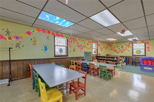 recreation room featuring a wainscoted wall, wooden walls, and a drop ceiling