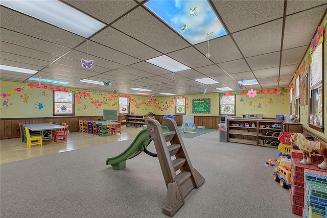 playroom with carpet floors, a wainscoted wall, and a drop ceiling