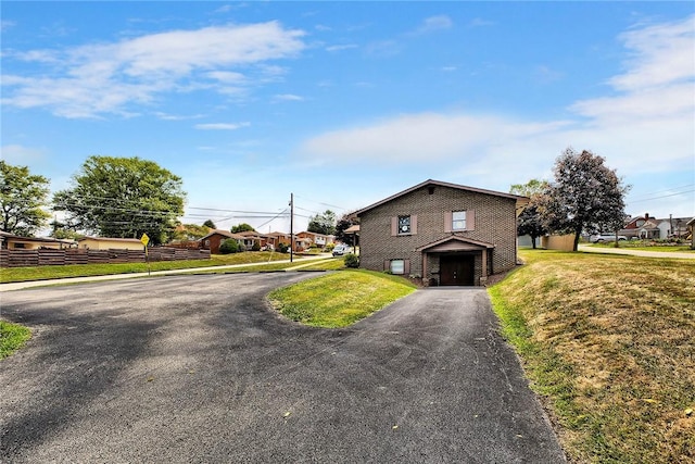 view of front of property featuring aphalt driveway, a front lawn, fence, and brick siding