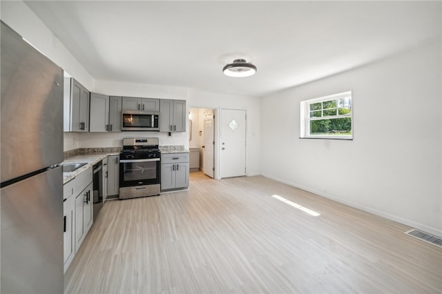 kitchen with sink, appliances with stainless steel finishes, light wood-type flooring, and gray cabinetry