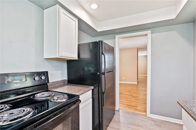 kitchen featuring white cabinetry, black appliances, light hardwood / wood-style flooring, and a tray ceiling