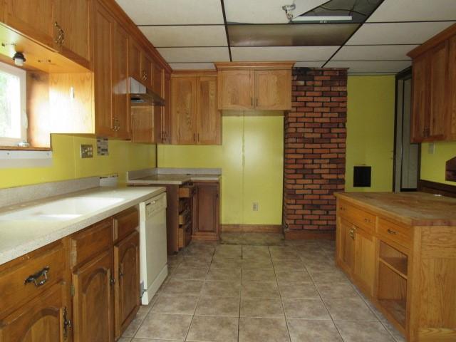 kitchen with light tile patterned flooring, brick wall, dishwasher, and a drop ceiling