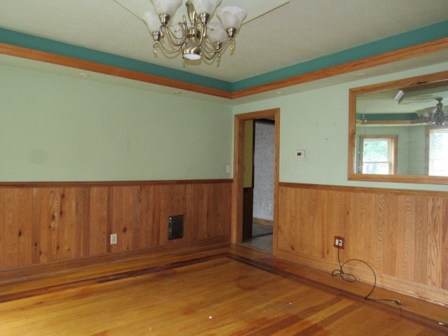 unfurnished room with wood walls, a chandelier, and hardwood / wood-style flooring