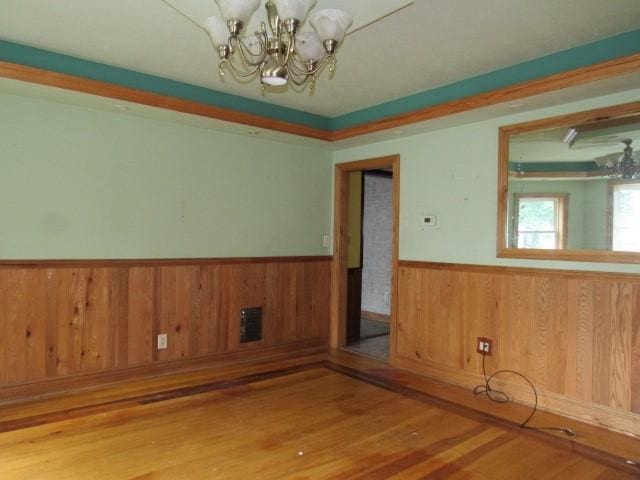 unfurnished room featuring wood walls, hardwood / wood-style floors, and a notable chandelier