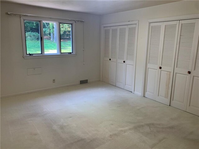 unfurnished bedroom featuring multiple closets and light carpet