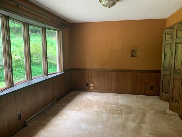 spare room featuring wood walls, a baseboard heating unit, and light colored carpet