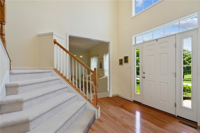 entryway featuring a towering ceiling, ornamental molding, and light wood-type flooring