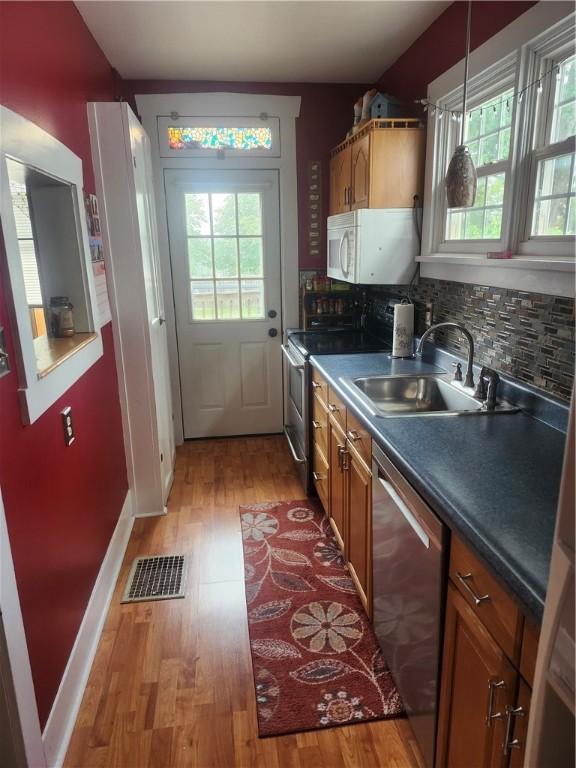 kitchen featuring appliances with stainless steel finishes, light hardwood / wood-style flooring, tasteful backsplash, and pendant lighting