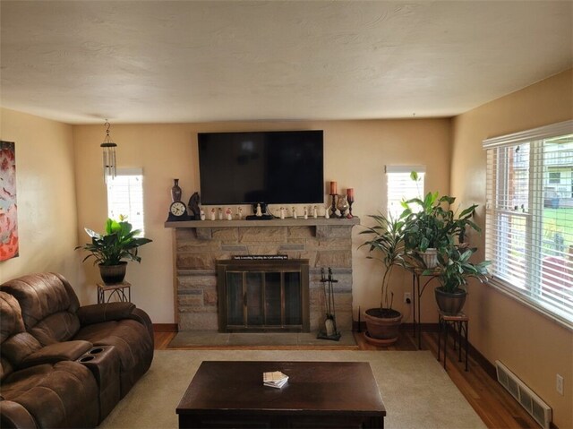 living room featuring hardwood / wood-style flooring, a stone fireplace, and plenty of natural light