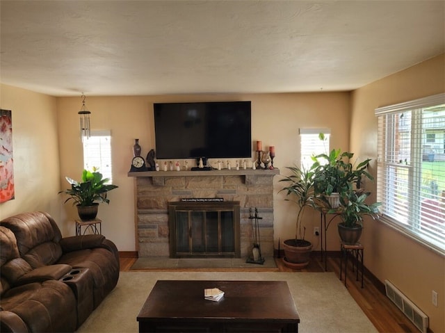 living area with a wealth of natural light, visible vents, a stone fireplace, and wood finished floors