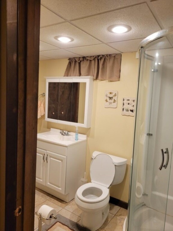 bathroom with a drop ceiling, vanity, tile patterned floors, an enclosed shower, and toilet