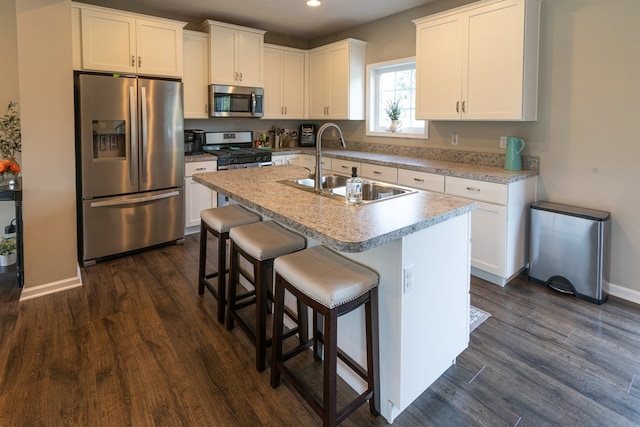 kitchen featuring dark hardwood / wood-style floors, sink, white cabinets, a center island with sink, and appliances with stainless steel finishes