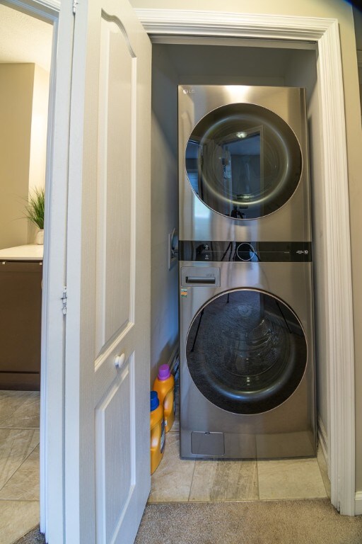 laundry room featuring stacked washer and dryer and light tile patterned floors