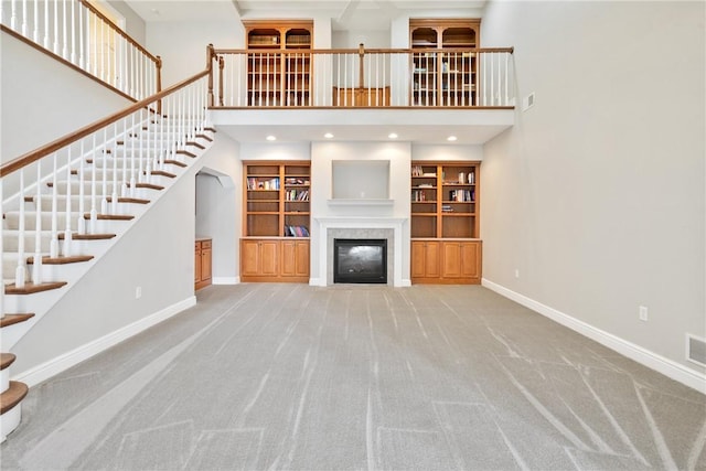 unfurnished living room with carpet flooring, a tile fireplace, a towering ceiling, and built in shelves