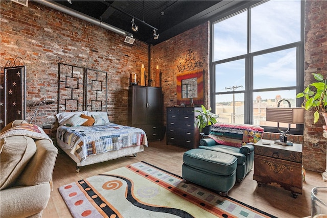 bedroom featuring track lighting, brick wall, and a towering ceiling