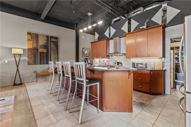 kitchen with light tile patterned flooring, backsplash, a kitchen island with sink, and wall chimney exhaust hood