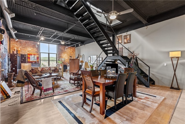 dining area featuring brick wall, light hardwood / wood-style flooring, ceiling fan, and a high ceiling