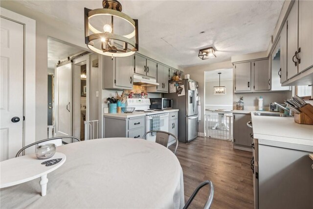 kitchen with hanging light fixtures, dark hardwood / wood-style flooring, sink, a barn door, and appliances with stainless steel finishes