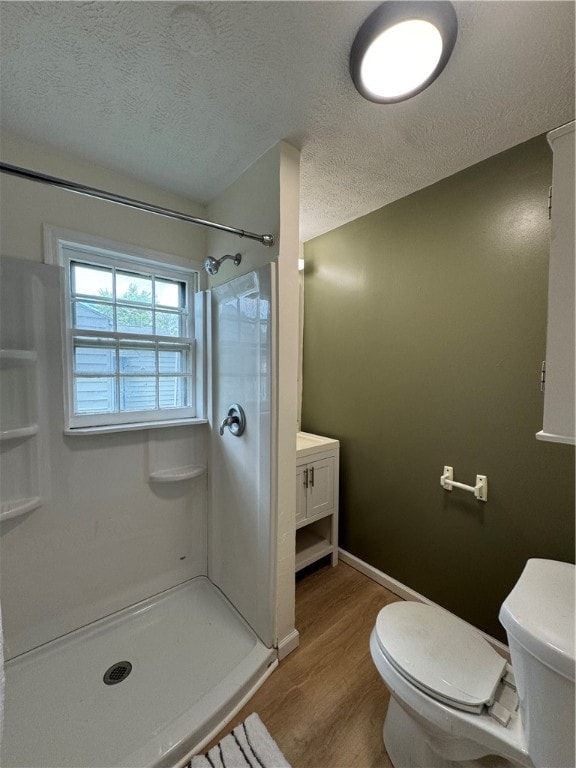 bathroom featuring vanity, hardwood / wood-style flooring, walk in shower, toilet, and a textured ceiling