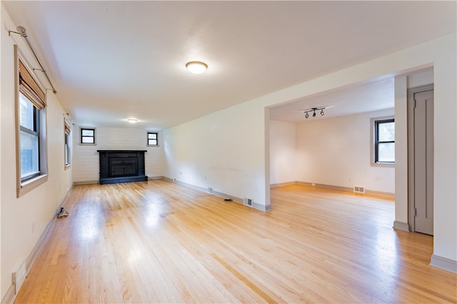 unfurnished living room featuring light wood-type flooring and a brick fireplace