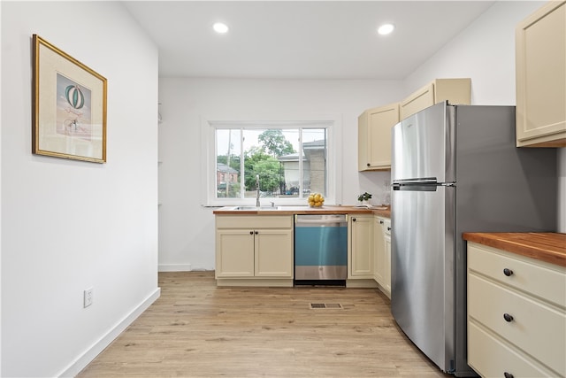 kitchen with appliances with stainless steel finishes, cream cabinetry, light hardwood / wood-style floors, butcher block countertops, and sink