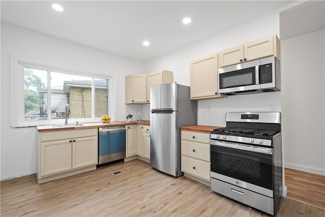 kitchen featuring light wood-type flooring, sink, butcher block counters, appliances with stainless steel finishes, and cream cabinets