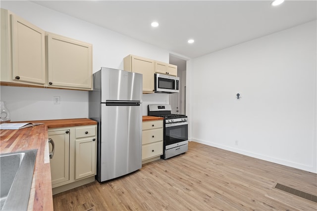 kitchen with cream cabinetry, butcher block counters, light hardwood / wood-style flooring, and stainless steel appliances