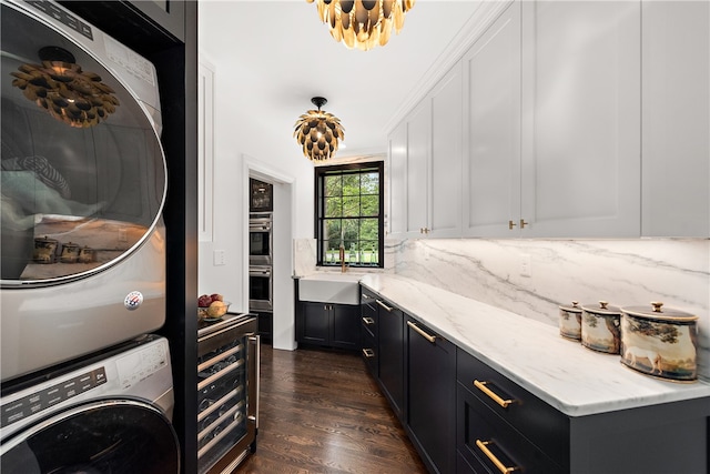 laundry room featuring stacked washer / drying machine, dark hardwood / wood-style flooring, cabinets, sink, and ornamental molding