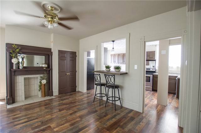 kitchen featuring stainless steel electric stove, hanging light fixtures, ceiling fan, dark hardwood / wood-style floors, and a kitchen bar