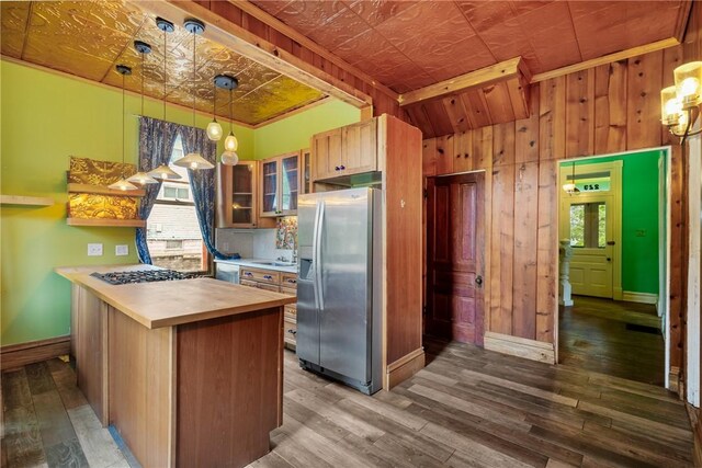 kitchen featuring plenty of natural light, wooden walls, hanging light fixtures, hardwood / wood-style flooring, and stainless steel fridge