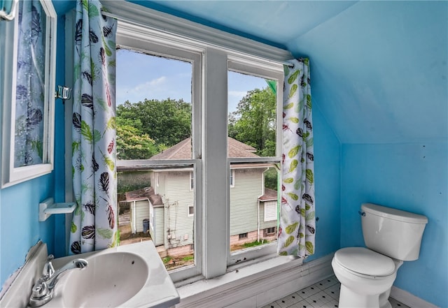 bathroom with a wealth of natural light, lofted ceiling, toilet, and tile patterned flooring