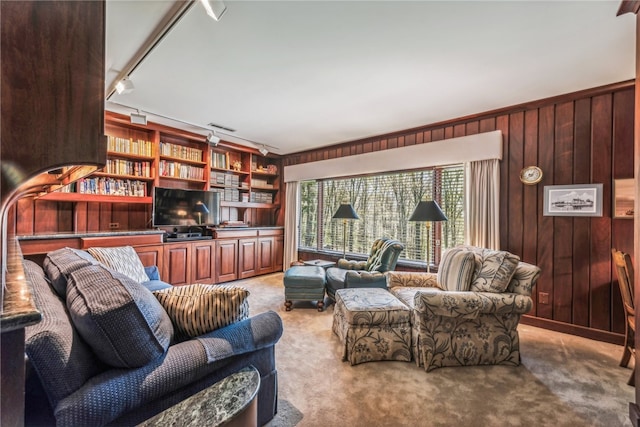 carpeted living room featuring wood walls, built in shelves, and rail lighting