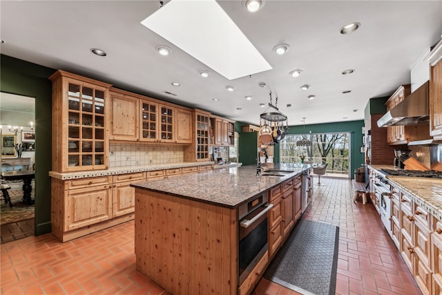 kitchen featuring dark stone countertops, decorative backsplash, appliances with stainless steel finishes, an island with sink, and sink