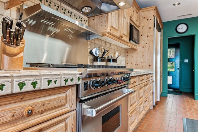 kitchen featuring designer stove, premium range hood, decorative backsplash, and light brown cabinets