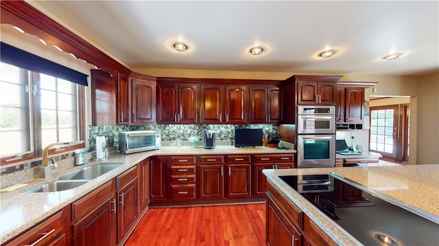 kitchen featuring stainless steel double oven, sink, backsplash, light hardwood / wood-style flooring, and light stone counters