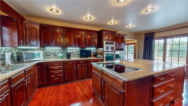 kitchen with tasteful backsplash, dark hardwood / wood-style flooring, stainless steel double oven, a center island, and black electric cooktop