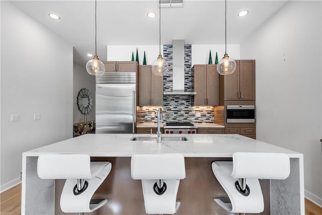 kitchen with built in refrigerator, a sink, wall chimney exhaust hood, decorative backsplash, and baseboards