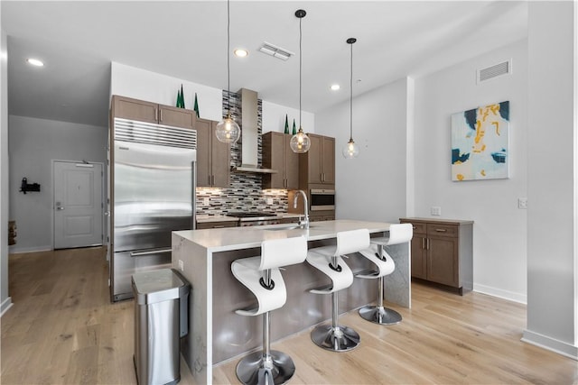 kitchen featuring stainless steel built in refrigerator, wall chimney exhaust hood, a sink, oven, and backsplash