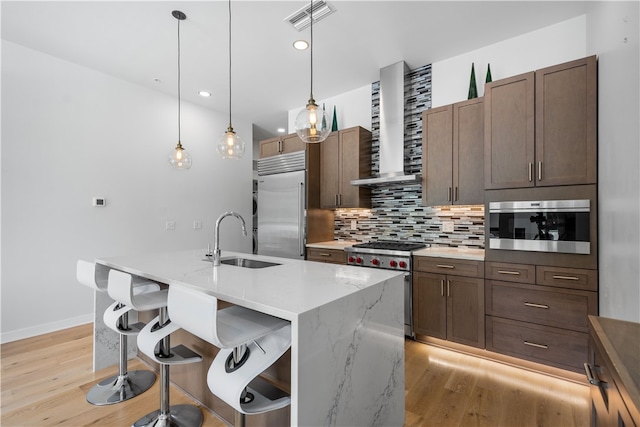 kitchen featuring high end appliances, light stone countertops, light hardwood / wood-style floors, sink, and wall chimney exhaust hood