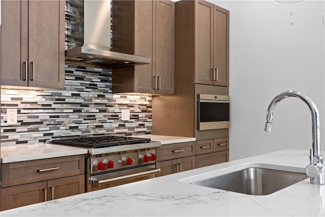 kitchen with tasteful backsplash, stainless steel appliances, sink, light stone countertops, and wall chimney exhaust hood